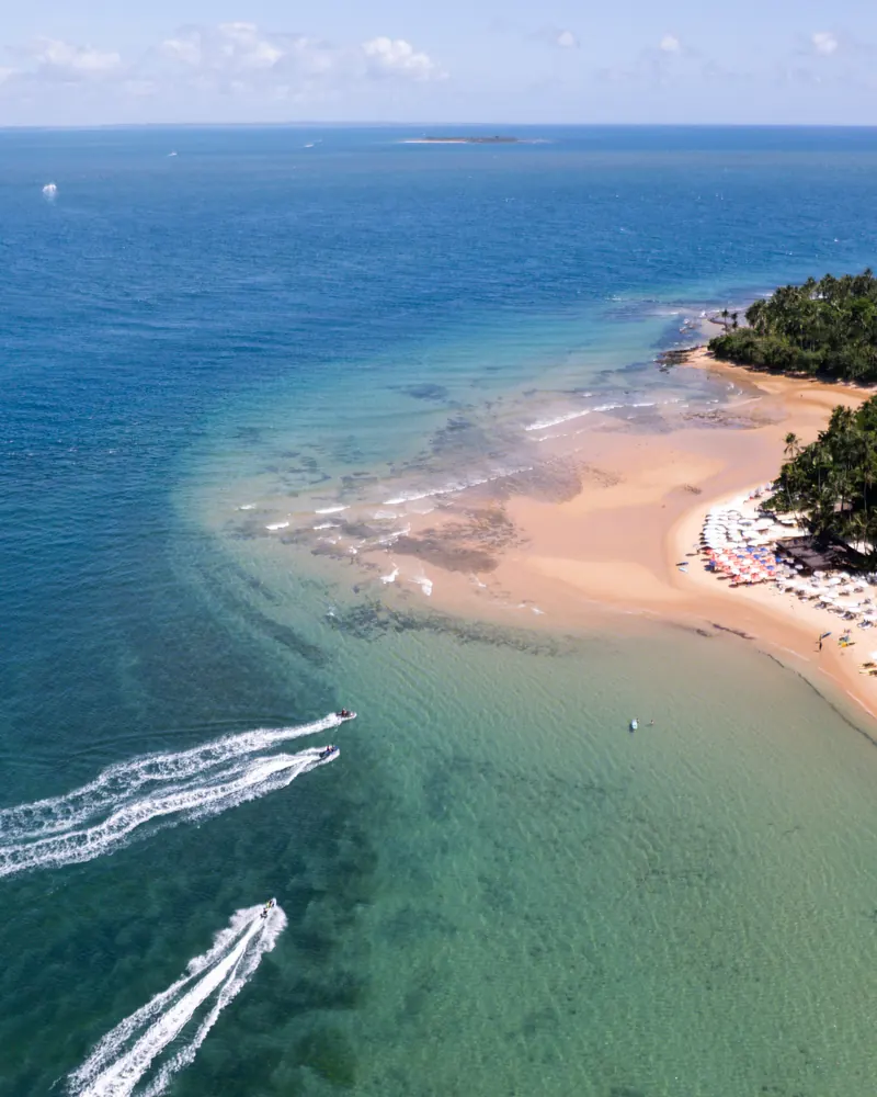 Ponta de areia com mar verde-claro e lanchas, vista do alto