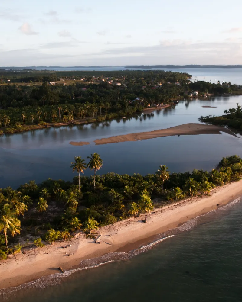 Faixa de areia com coqueiros entre a lagoa e o mar, ao entardecer